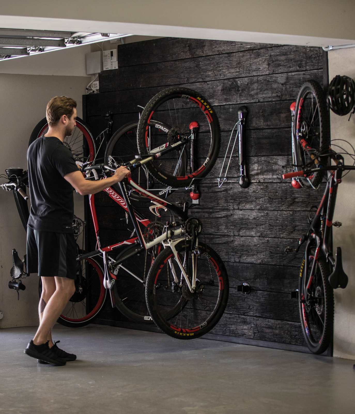 A person in a garage loading a mountain bike into a Steadyrack bike rack alongside other stored bikes.