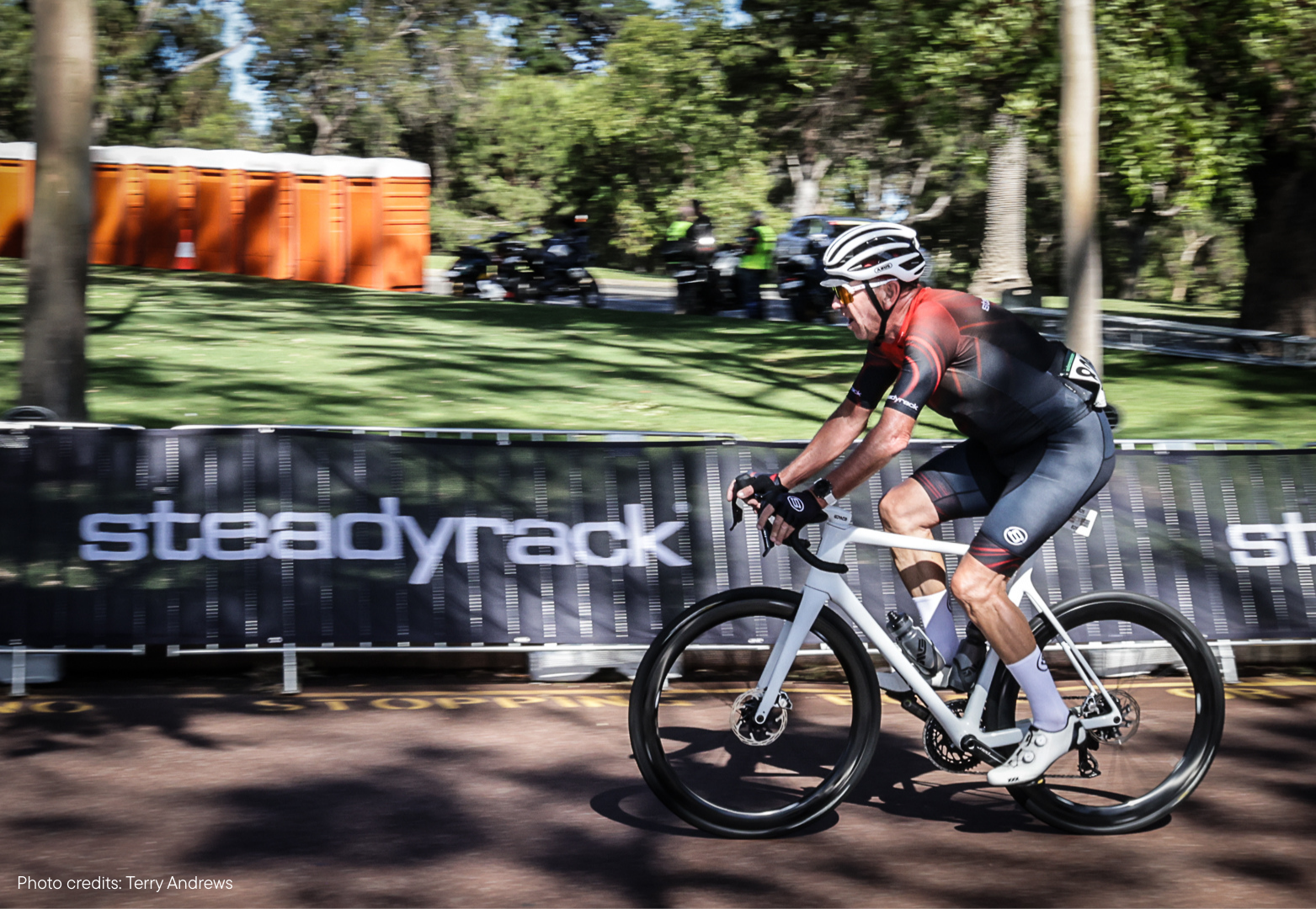 A cyclist in motion on a gravel road with a grass background with trees.